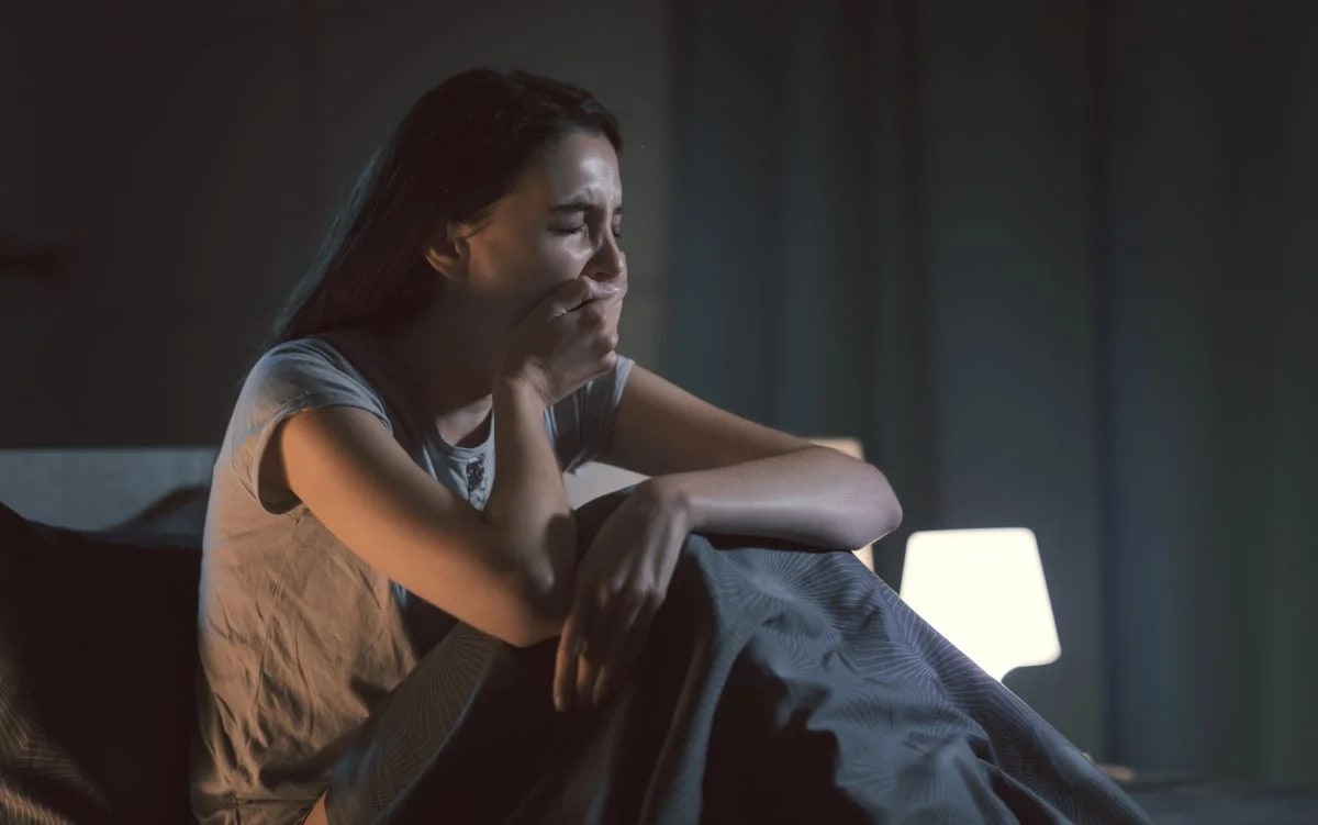 Mulher deitada na cama de madrugada acordada com expressão cansada, retrato de insônia crônica
