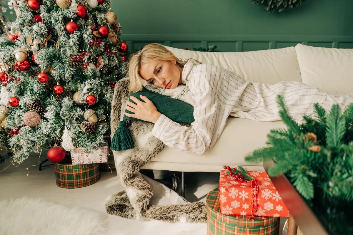 Mulher pensativa diante de árvore de Natal ilustrando melancolia e depressão de fim de ano