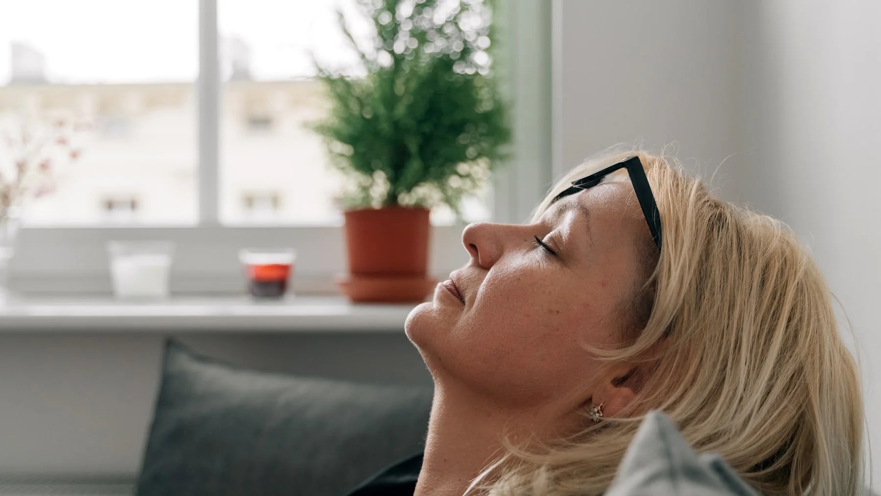 Mulher relaxando de olhos fechados no sofá, num momento de descanso.