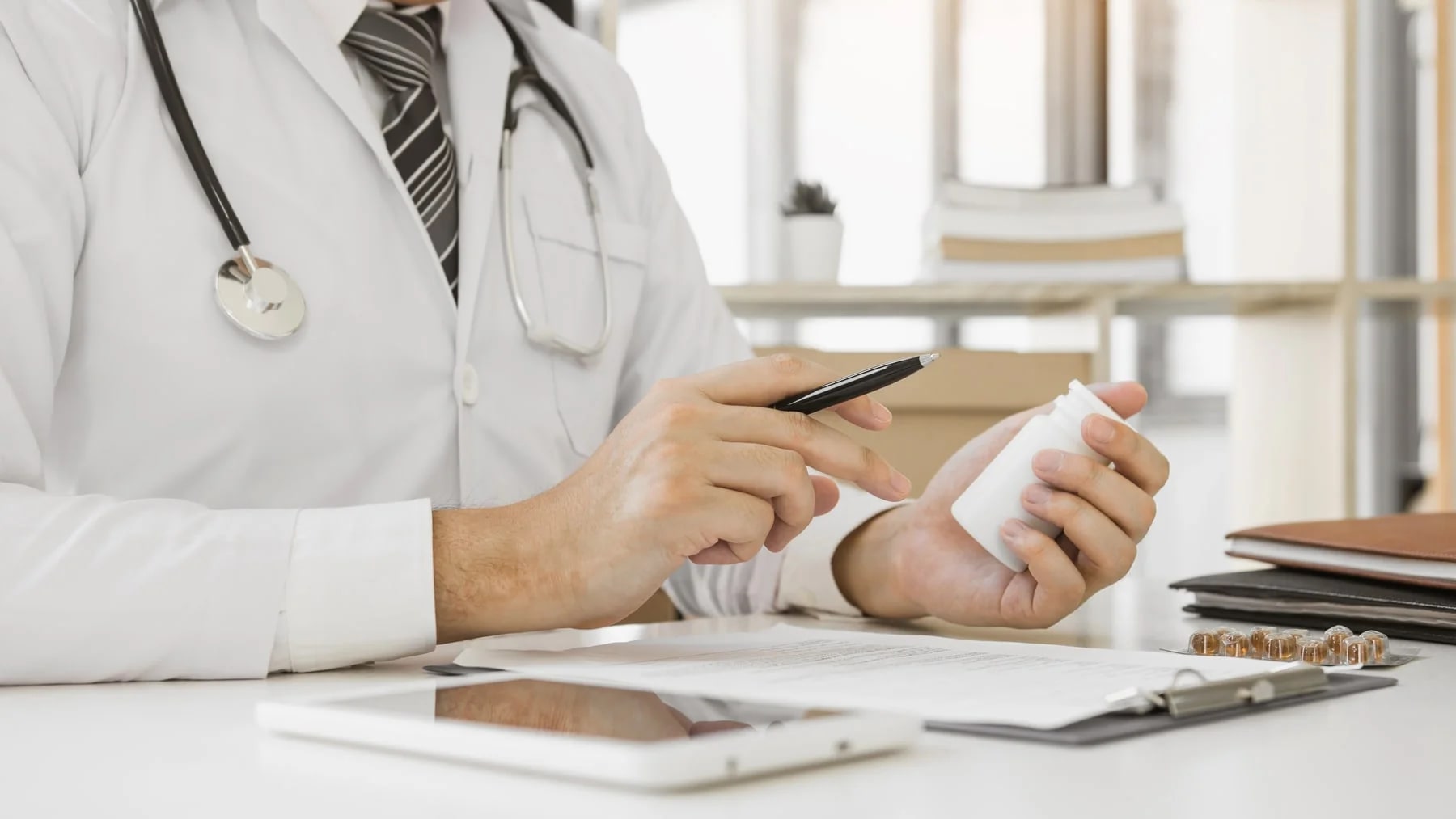 Médico à mesa do consultório avaliando um frasco durante a consulta.