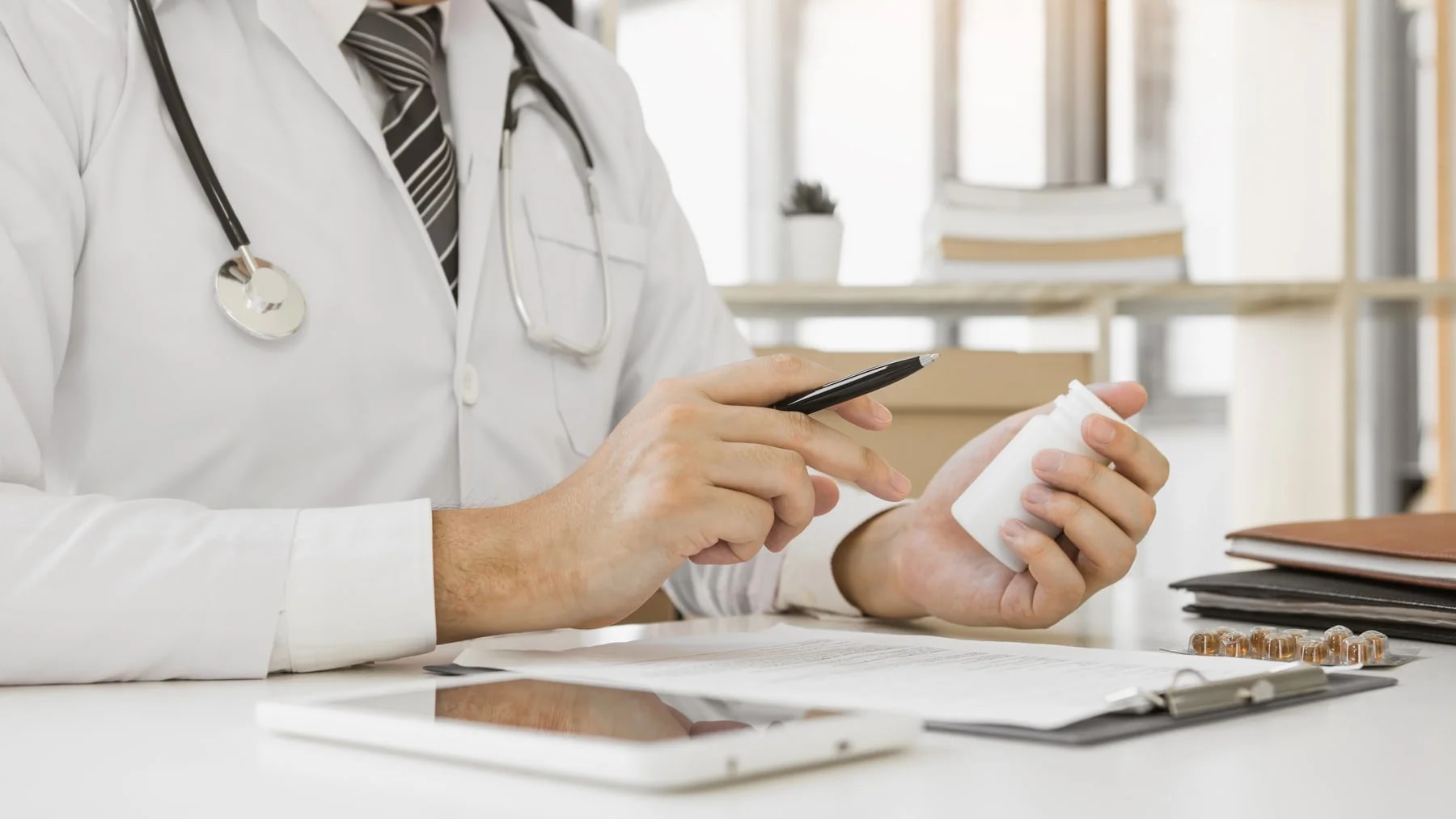 Médico à mesa do consultório avaliando um frasco durante a consulta.