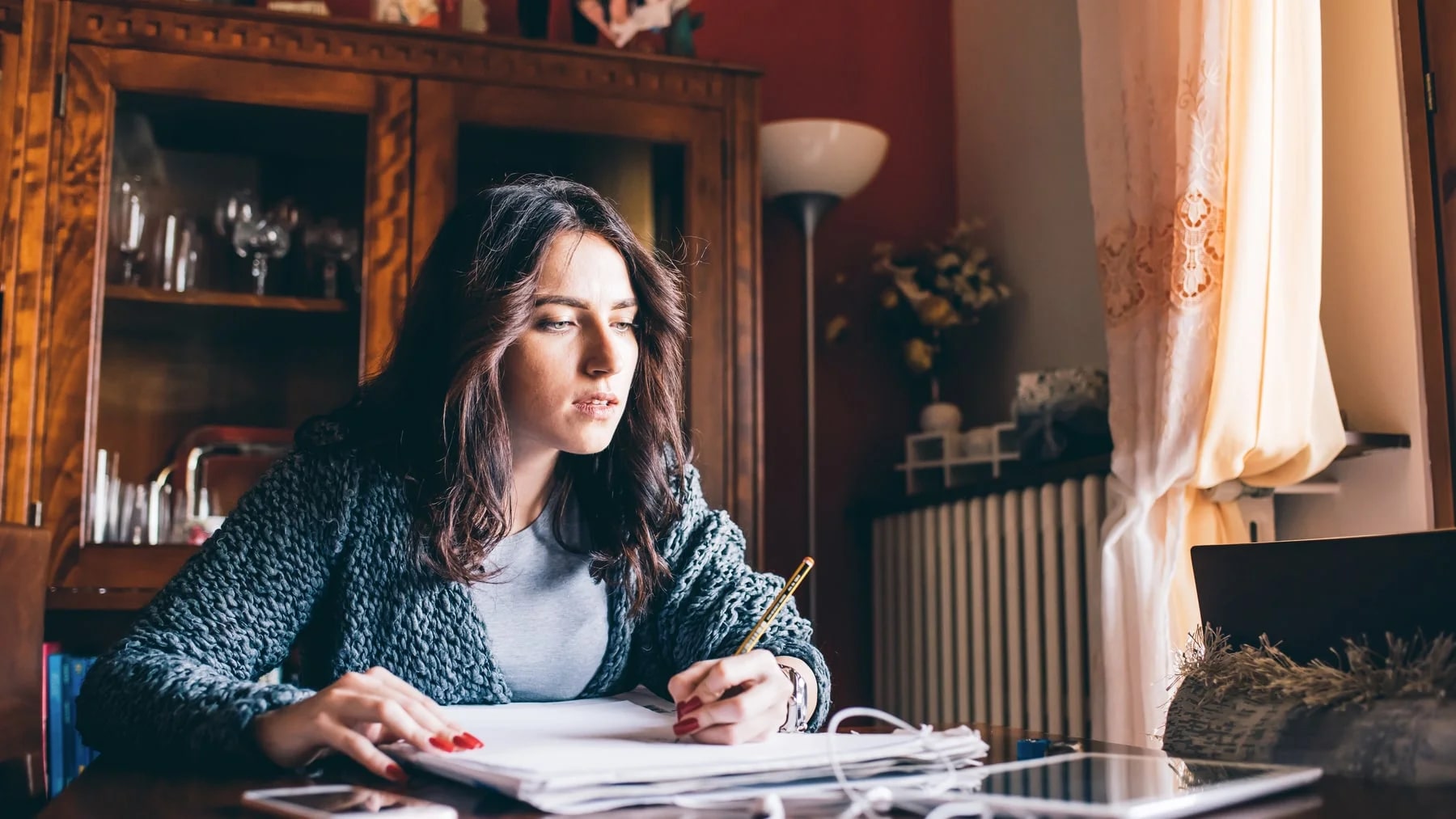 Mulher concentrada organizando papéis e anotações na mesa de casa, sob luz natural.