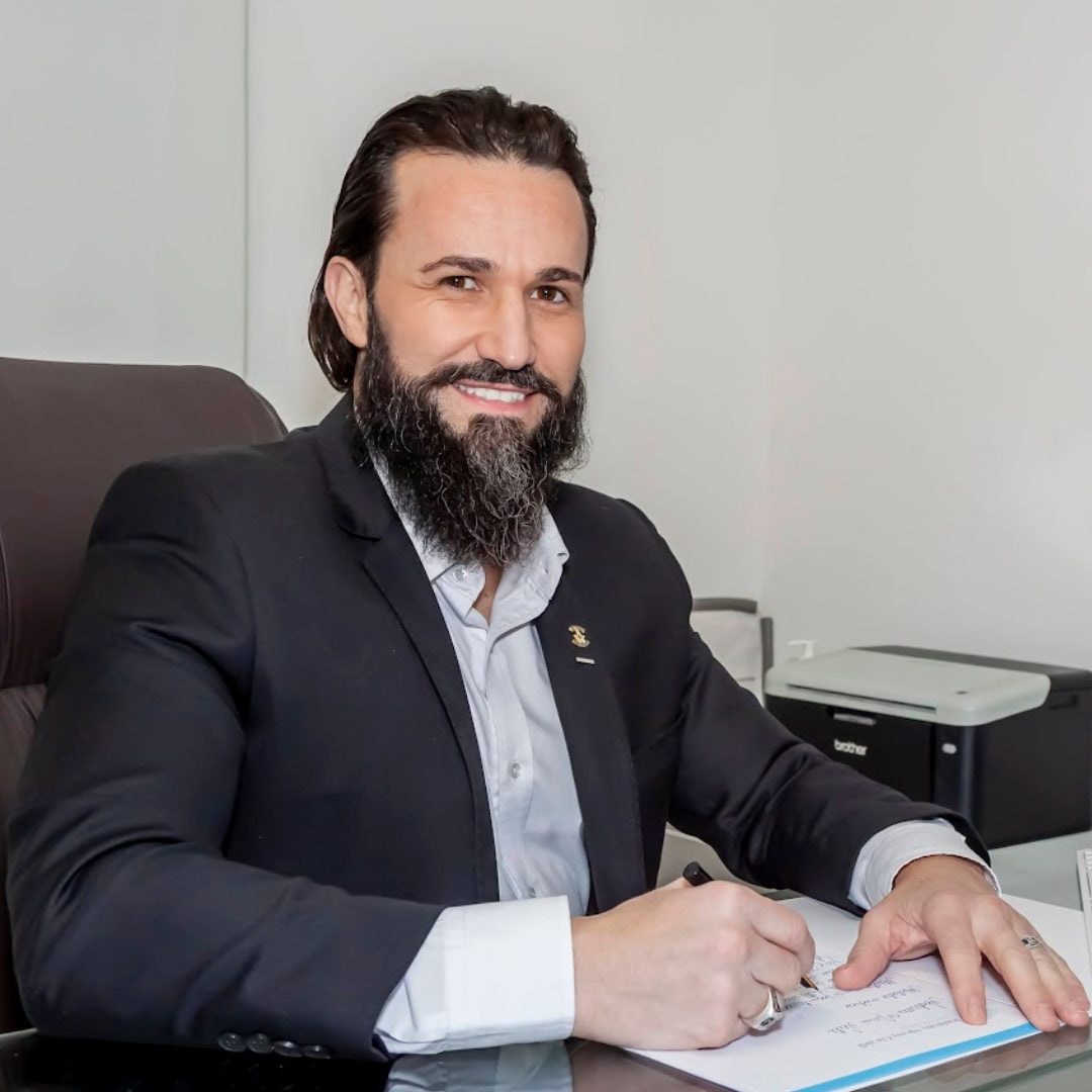 Dr. Rodrigo Rocha assinando laudo no consultório do Instituto Alceu Giraldi, paletó preto e insígnia oficial de perito
