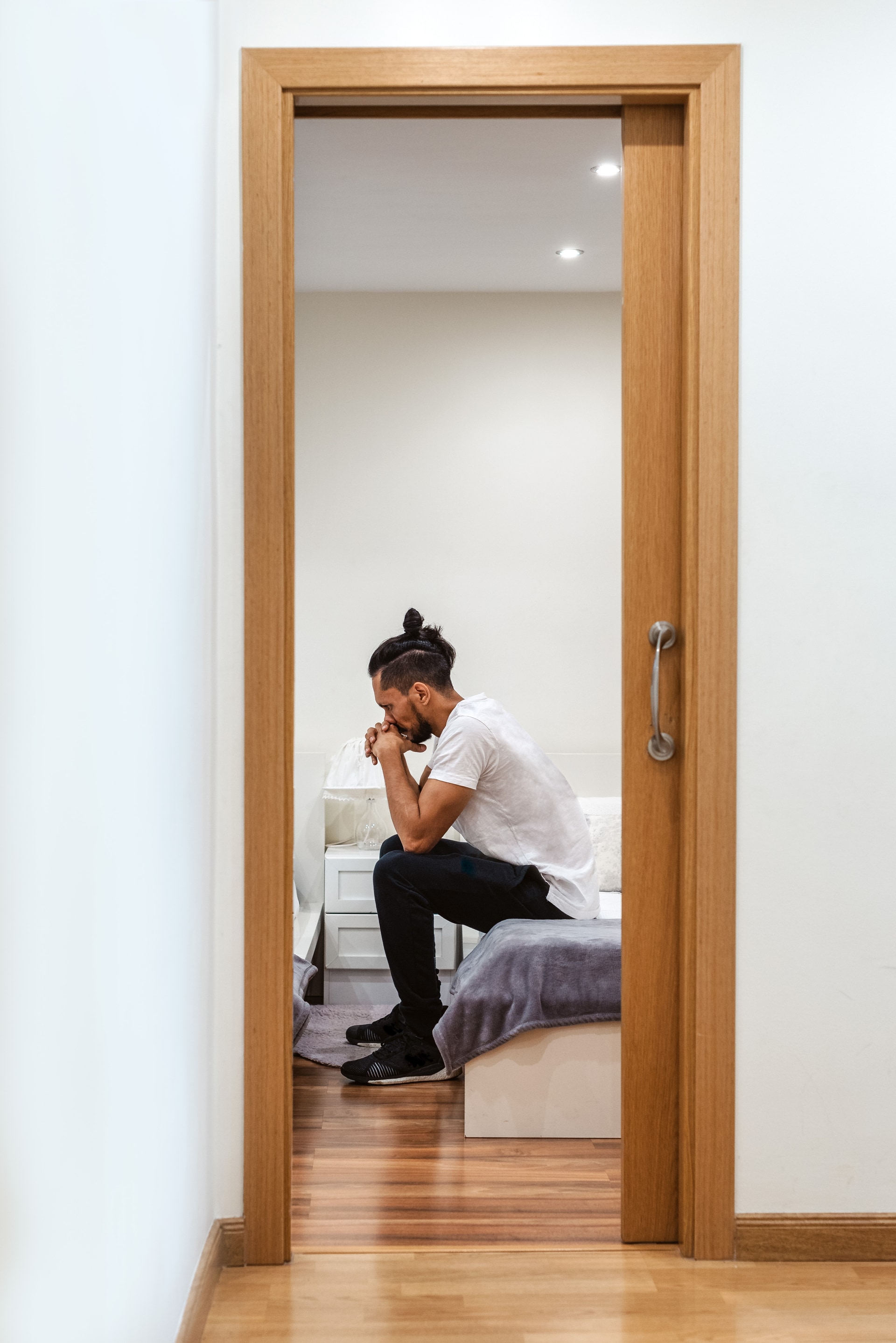 Homem sentado na beira da cama, cabisbaixo, em momento de recolhimento. Imagem editorial sobre depressão no Instituto Alceu Giraldi.