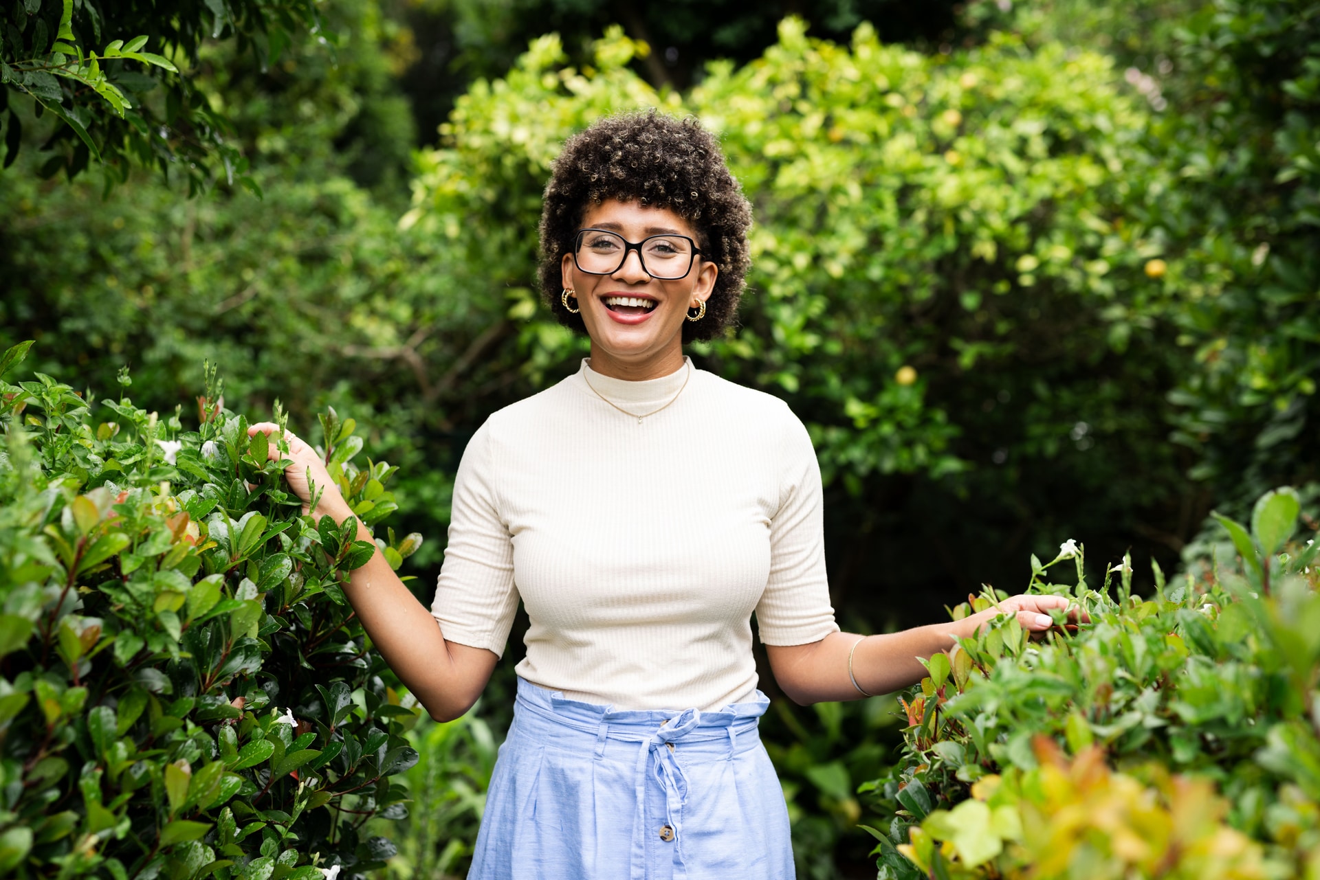 Mulher sorrindo entre arbustos verdes em jardim ensolarado. Imagem editorial sobre transtorno bipolar no Instituto Alceu Giraldi.